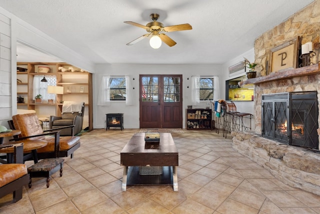 tiled living room featuring ceiling fan, a stone fireplace, and a textured ceiling