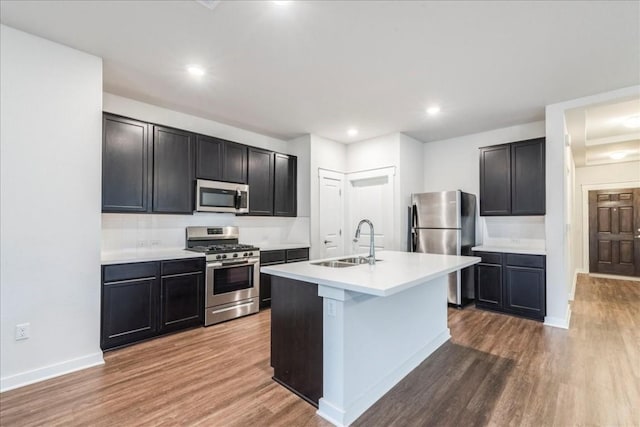 kitchen featuring an island with sink, appliances with stainless steel finishes, wood finished floors, light countertops, and a sink