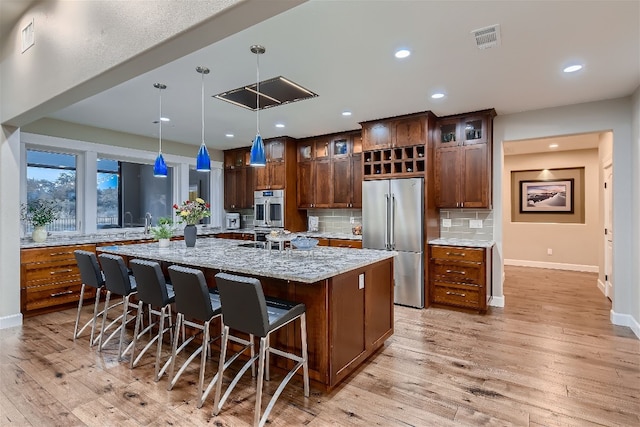 kitchen featuring appliances with stainless steel finishes, a center island with sink, a breakfast bar area, light stone countertops, and pendant lighting