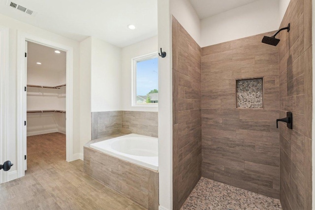 bathroom featuring wood finished floors, a stall shower, a spacious closet, a bath, and visible vents