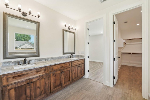 full bath with a spacious closet, wood finished floors, a sink, and double vanity