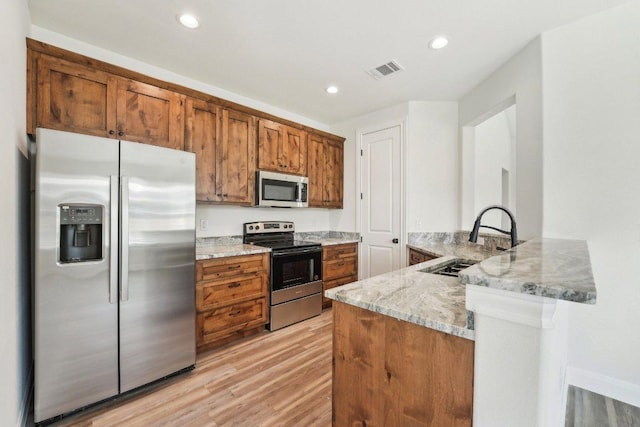 kitchen featuring brown cabinetry, light wood-type flooring, stainless steel appliances, light stone countertops, and visible vents