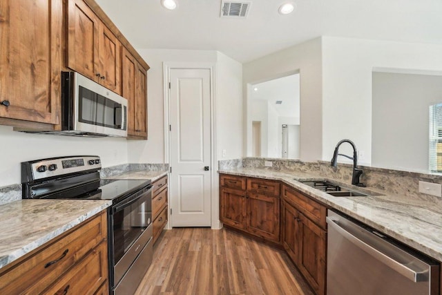 kitchen featuring a sink, brown cabinets, light wood-style floors, stainless steel appliances, and visible vents