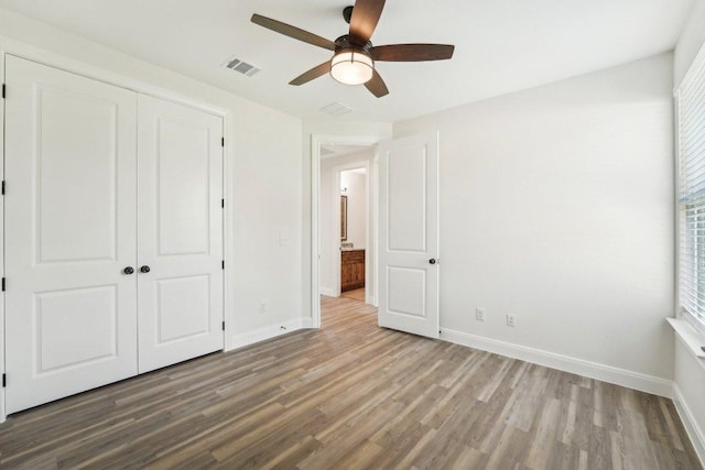 unfurnished bedroom featuring baseboards, wood finished floors, visible vents, and a closet