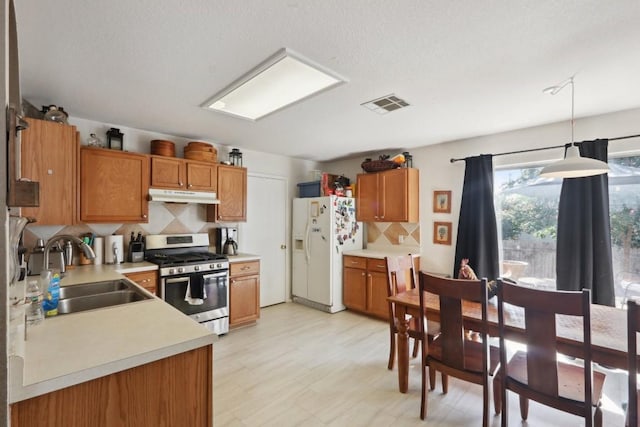 17405 Wiseman Dr, Pflugerville, TX 78660 - kitchen featuring white refrigerator with ice dispenser, stainless steel range with gas cooktop, a sink, under cabinet range hood, and brown cabinets
