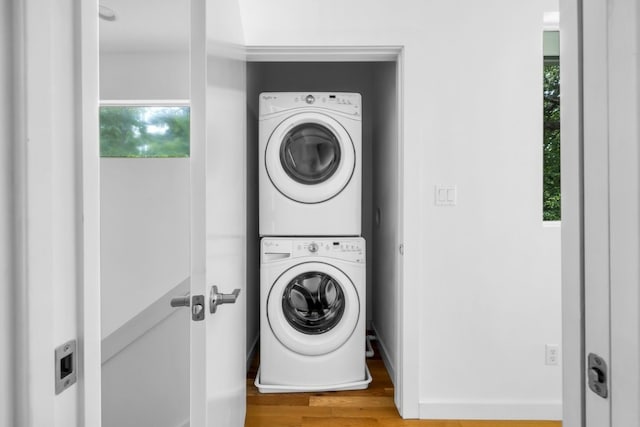 clothes washing area featuring laundry area, baseboards, wood finished floors, and stacked washer and clothes dryer