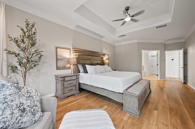 bedroom with a tray ceiling, light hardwood / wood-style flooring, ornamental molding, and connected bathroom