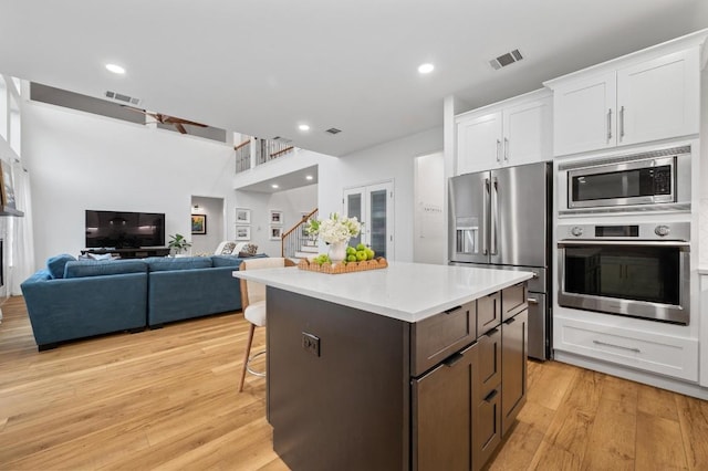 kitchen with stainless steel appliances, a center island, light hardwood / wood-style floors, white cabinets, and a kitchen bar