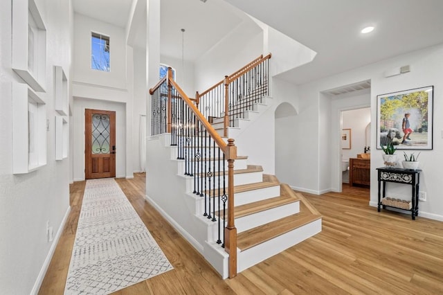 entryway featuring a notable chandelier, a towering ceiling, and light hardwood / wood-style floors