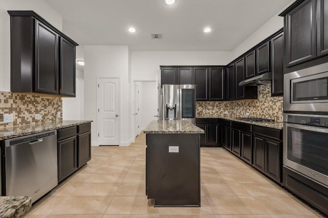 578 Ledge Stone Dr, Austin, TX 78737 - kitchen with stainless steel appliances, under cabinet range hood, light stone counters, a kitchen island, and decorative backsplash