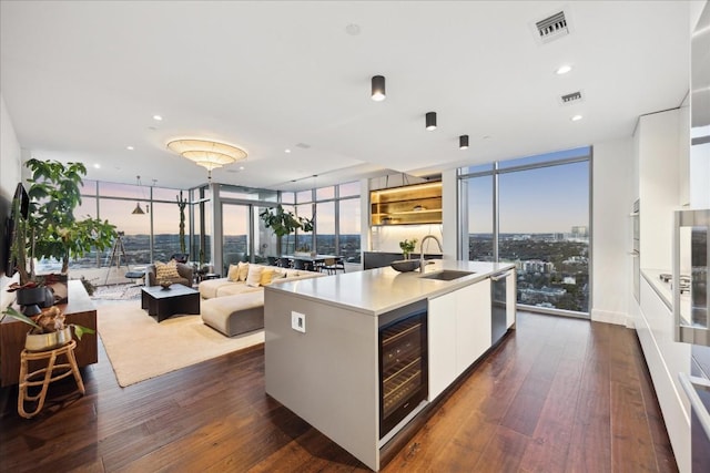 kitchen with a center island with sink, white cabinets, floor to ceiling windows, beverage cooler, and sink