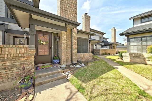 entrance to property with brick siding, a lawn, and a chimney