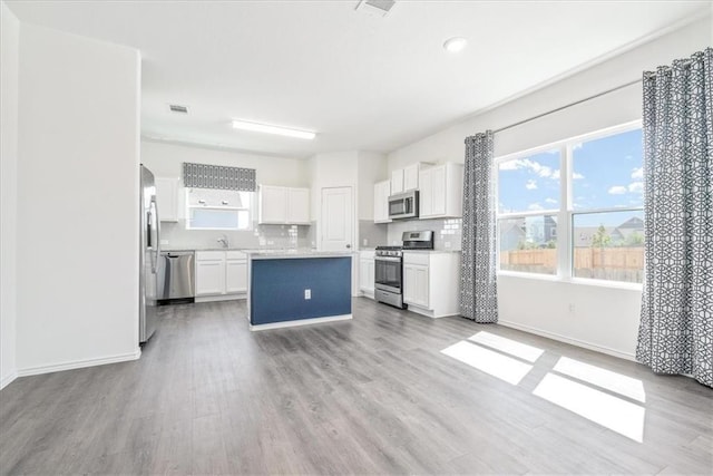 kitchen with light hardwood / wood-style flooring, a kitchen island, stainless steel appliances, white cabinets, and tasteful backsplash