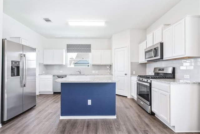 kitchen with wood-type flooring, white cabinetry, a kitchen island, stainless steel appliances, and decorative backsplash
