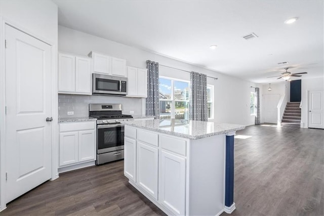 kitchen featuring appliances with stainless steel finishes, white cabinetry, a center island, and light stone counters