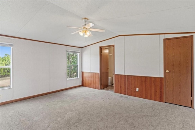 spare room featuring wooden walls, light carpet, vaulted ceiling, and crown molding