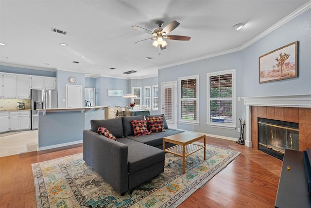 living room with ceiling fan, ornamental molding, a tile fireplace, and light hardwood / wood-style floors