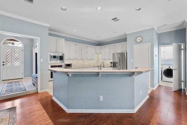 kitchen featuring appliances with stainless steel finishes, washer / clothes dryer, white cabinetry, and a kitchen island with sink