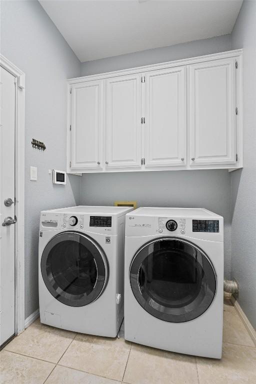 washroom featuring light tile patterned flooring, cabinets, and washing machine and clothes dryer