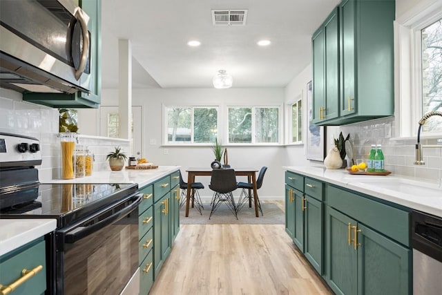 kitchen with green cabinets, stainless steel appliances, light hardwood / wood-style floors, sink, and decorative backsplash