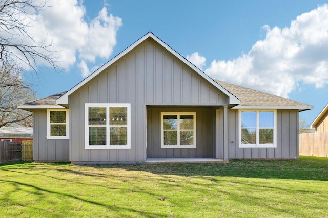 back of property featuring board and batten siding, fence, and a lawn