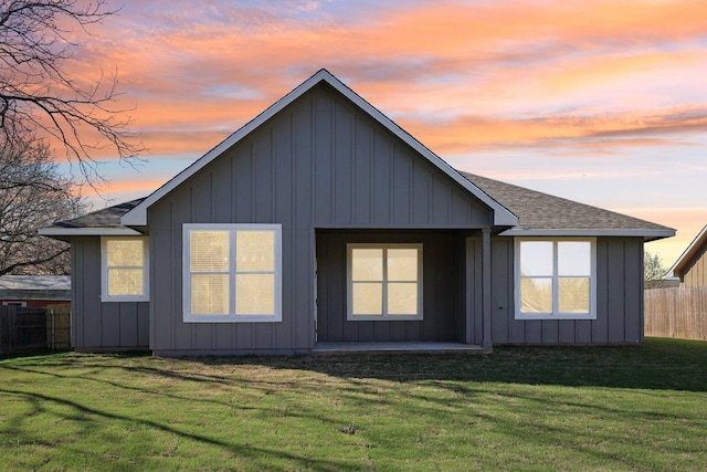 rear view of house with a lawn, fence, board and batten siding, and roof with shingles