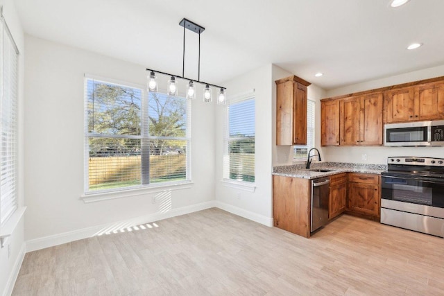 kitchen featuring light stone countertops, stainless steel appliances, a sink, light wood-style floors, and brown cabinetry