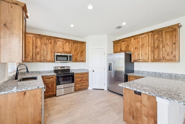 kitchen with a sink, light stone countertops, appliances with stainless steel finishes, visible vents, and light wood-style floors