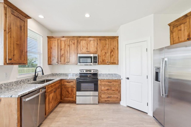 kitchen featuring a sink, light stone countertops, brown cabinets, stainless steel appliances, and recessed lighting
