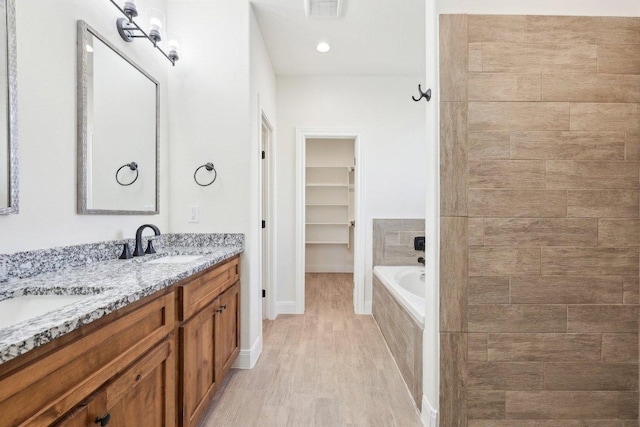 full bath featuring visible vents, a sink, a spacious closet, and wood finished floors