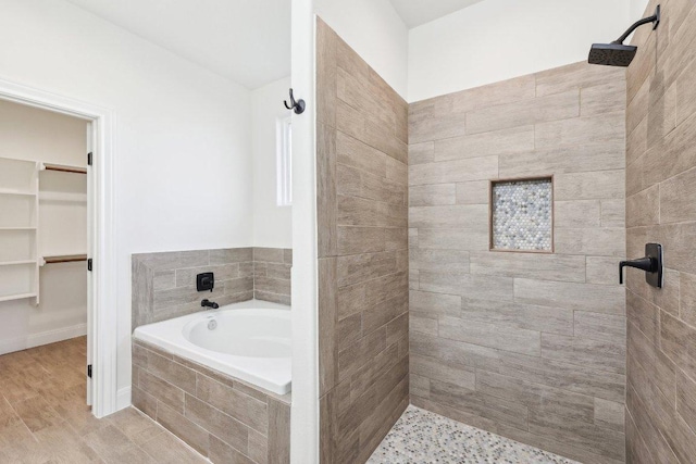 full bathroom with a tile shower, a garden tub, a walk in closet, and wood finished floors