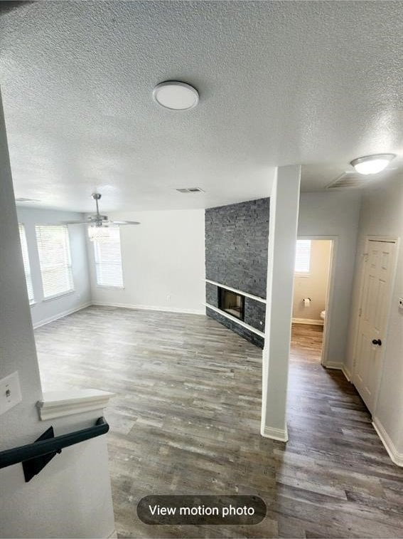 2500 National Park Blvd, Austin, TX 78747 - unfurnished living room with wood finished floors, a textured ceiling, a stone fireplace, and ceiling fan