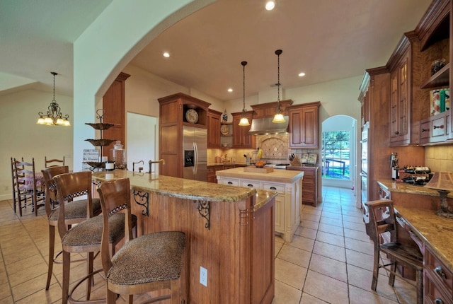 kitchen with hanging light fixtures, light stone counters, extractor fan, a center island, and stainless steel fridge with ice dispenser