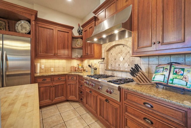 kitchen featuring appliances with stainless steel finishes, light tile patterned flooring, exhaust hood, butcher block countertops, and decorative backsplash