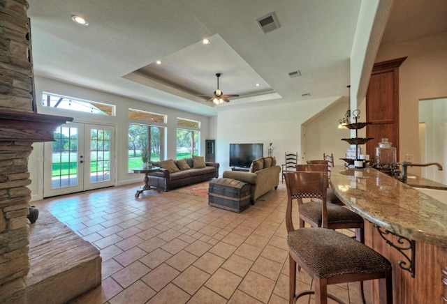 tiled living room with a tray ceiling, french doors, sink, and ceiling fan