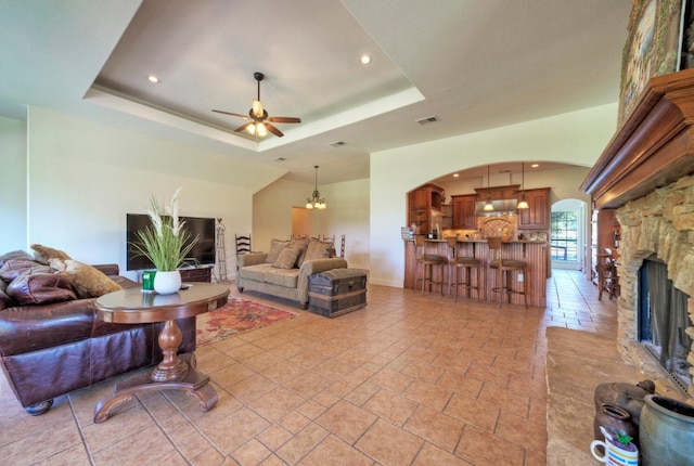 living room featuring a tray ceiling, ceiling fan, and a fireplace