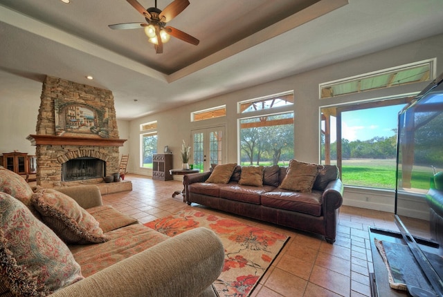 living room featuring french doors, ceiling fan, a fireplace, a tray ceiling, and light tile patterned floors