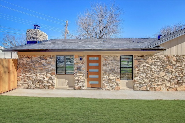 back of property with a yard, fence, stone siding, and a chimney