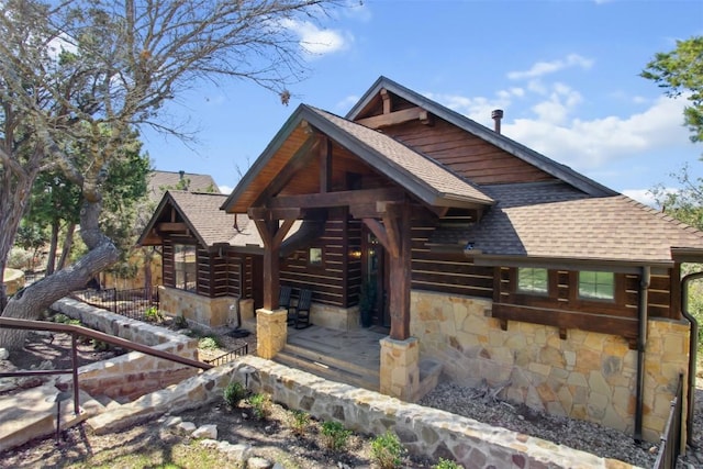 rear view of house with stone siding and roof with shingles