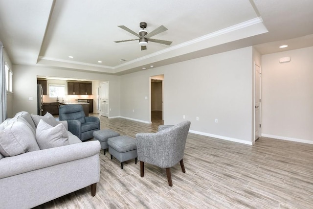 living room featuring ceiling fan, light hardwood / wood-style floors, a tray ceiling, and crown molding