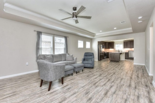 living room with ceiling fan, light hardwood / wood-style flooring, crown molding, and a raised ceiling