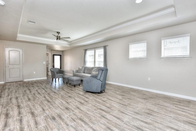 living room with ceiling fan, light wood-type flooring, crown molding, and a raised ceiling