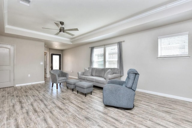 living room with crown molding, light wood-type flooring, a tray ceiling, and ceiling fan