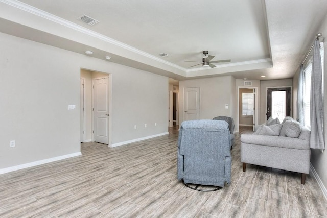 living room featuring light hardwood / wood-style floors, a tray ceiling, ornamental molding, and ceiling fan