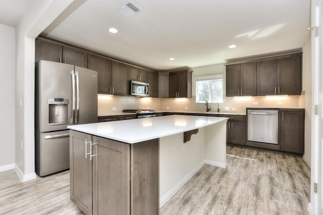 kitchen featuring backsplash, a center island, light hardwood / wood-style floors, stainless steel appliances, and dark brown cabinetry