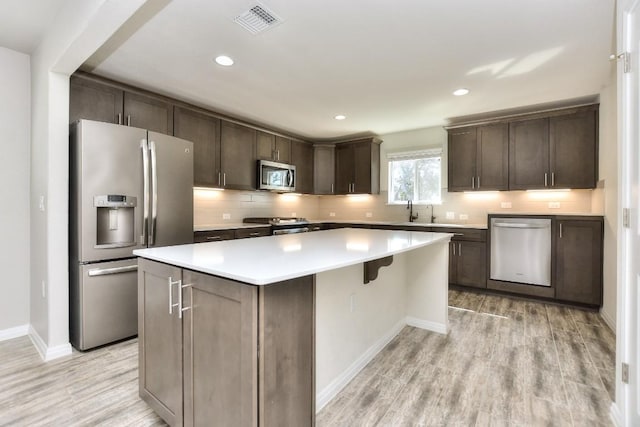 220 Comal Ln, Georgetown, TX 78633 - kitchen featuring appliances with stainless steel finishes, a kitchen island, light wood-style flooring, dark brown cabinetry, and light countertops
