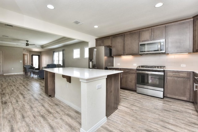 kitchen featuring a center island, light hardwood / wood-style floors, stainless steel appliances, dark brown cabinets, and decorative backsplash