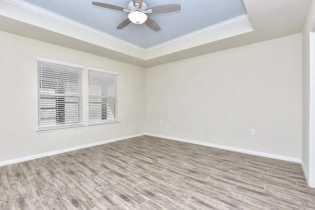 empty room featuring a tray ceiling, light hardwood / wood-style flooring, crown molding, and ceiling fan