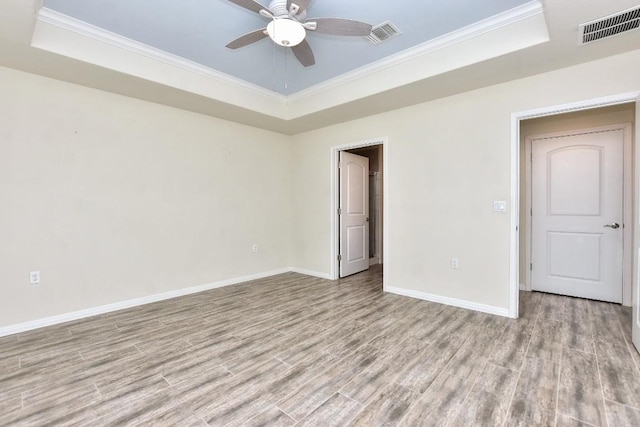 unfurnished room with a tray ceiling, ornamental molding, light wood-type flooring, and ceiling fan