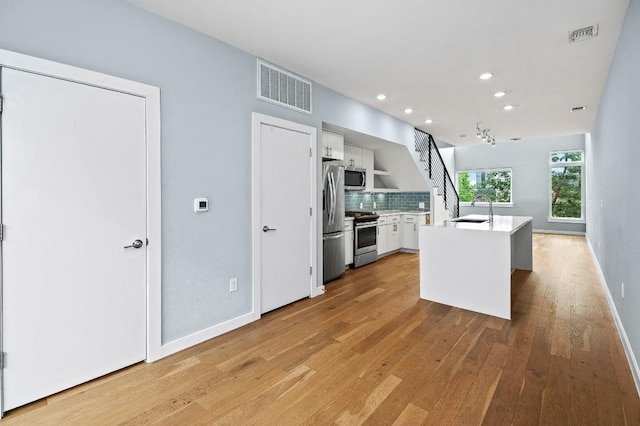 2002 E 7th St Unit 204, Austin, TX 78702 - kitchen with appliances with stainless steel finishes, a sink, white cabinetry, light wood-style flooring, and tasteful backsplash